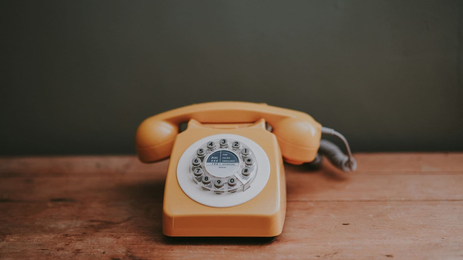 A brown rotary-dial telephone on a desk in a grey room