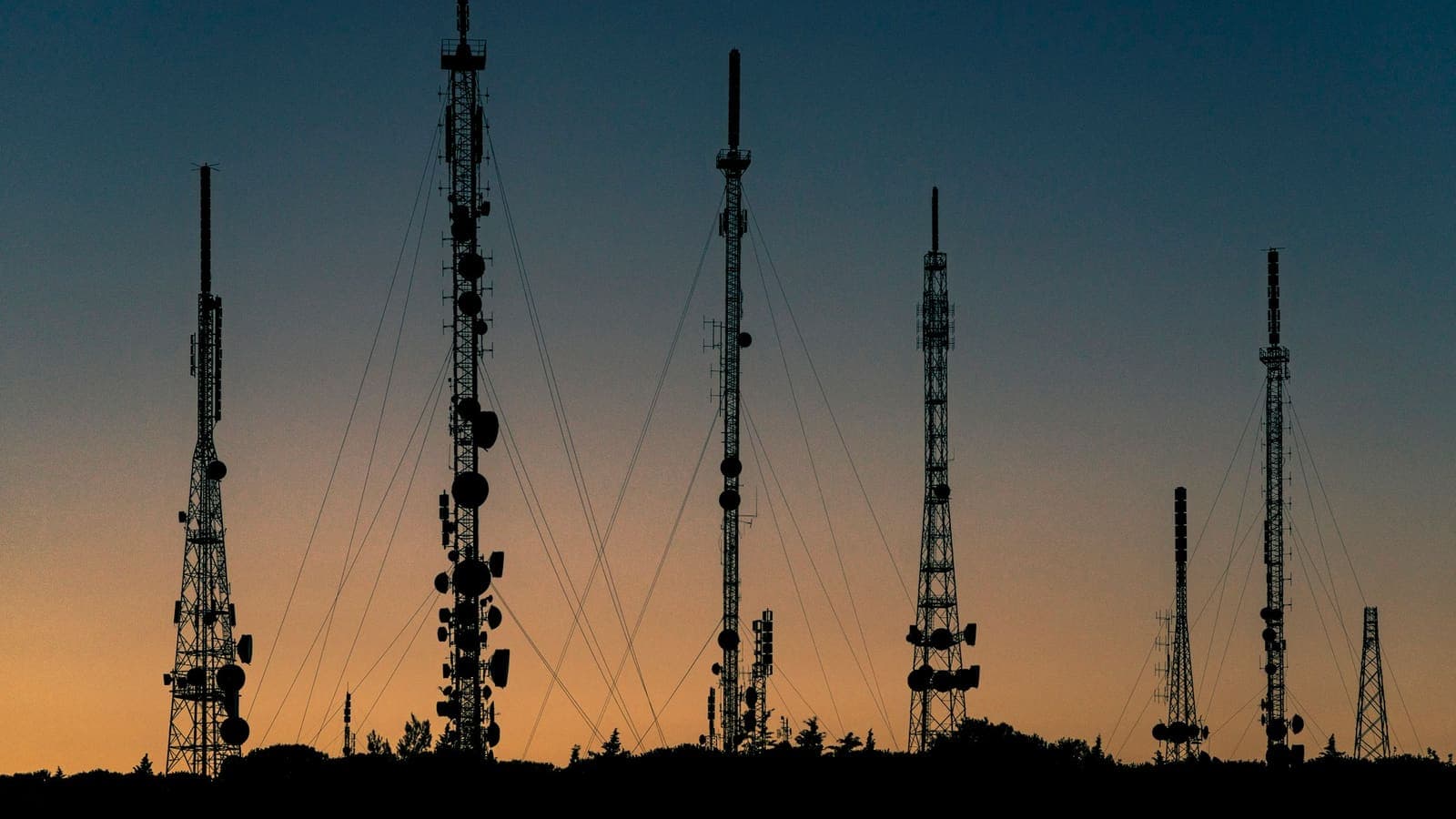 Des pylônes de télécommunication en silhouette sur un ciel de coucher de soleil