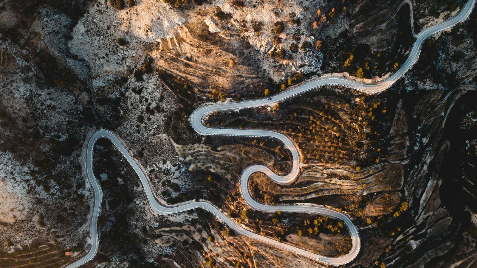 Aerial view of a road through dark forest — the route matters more than the speed