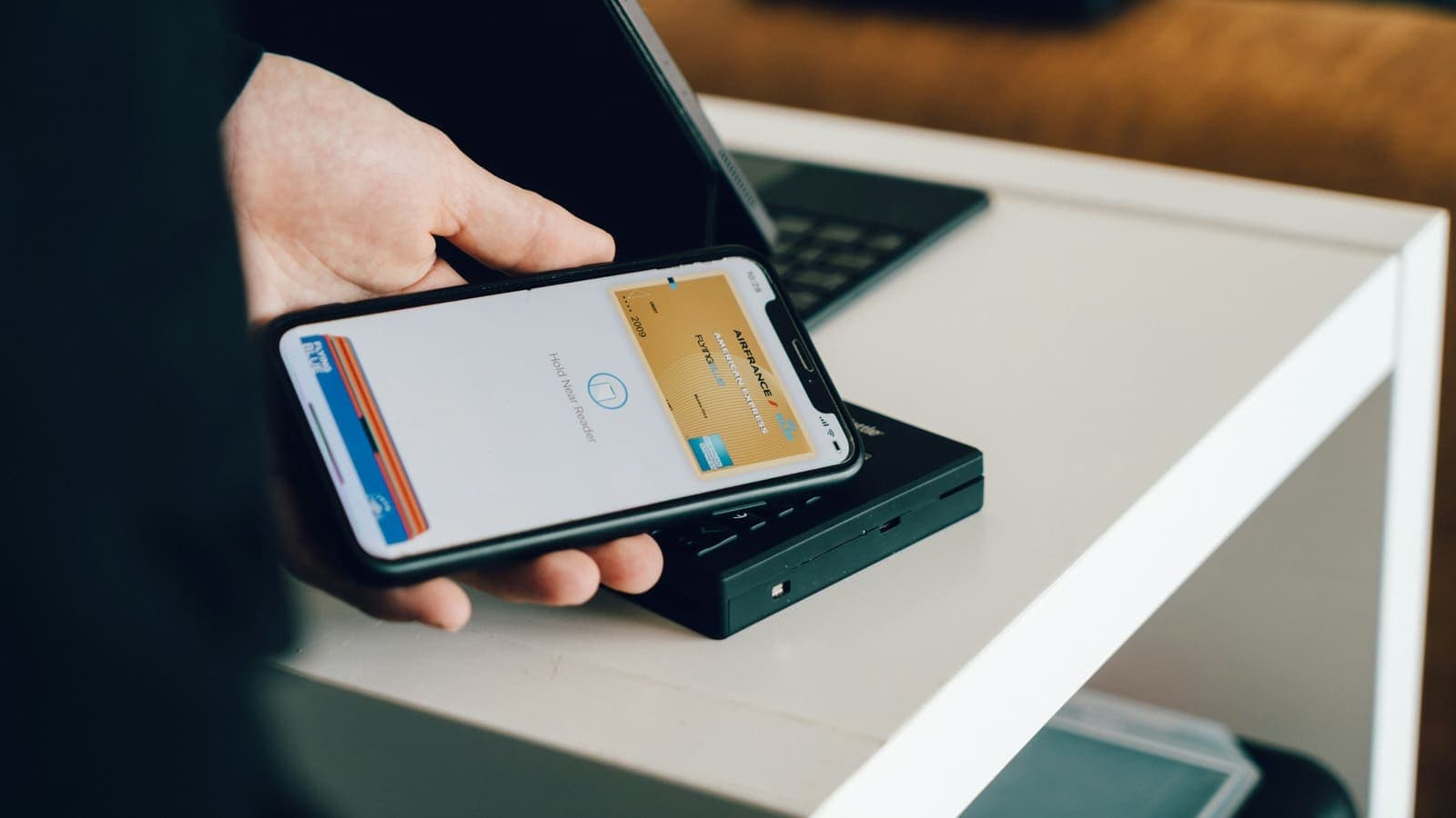 A hand holding a smartphone over a card reader for a contactless payment