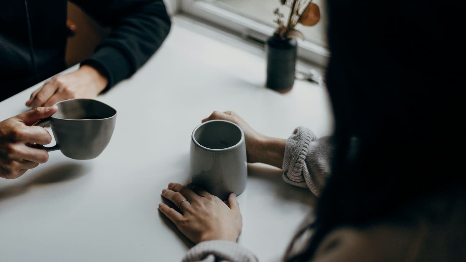 Two people holding grey mugs in conversation across a table