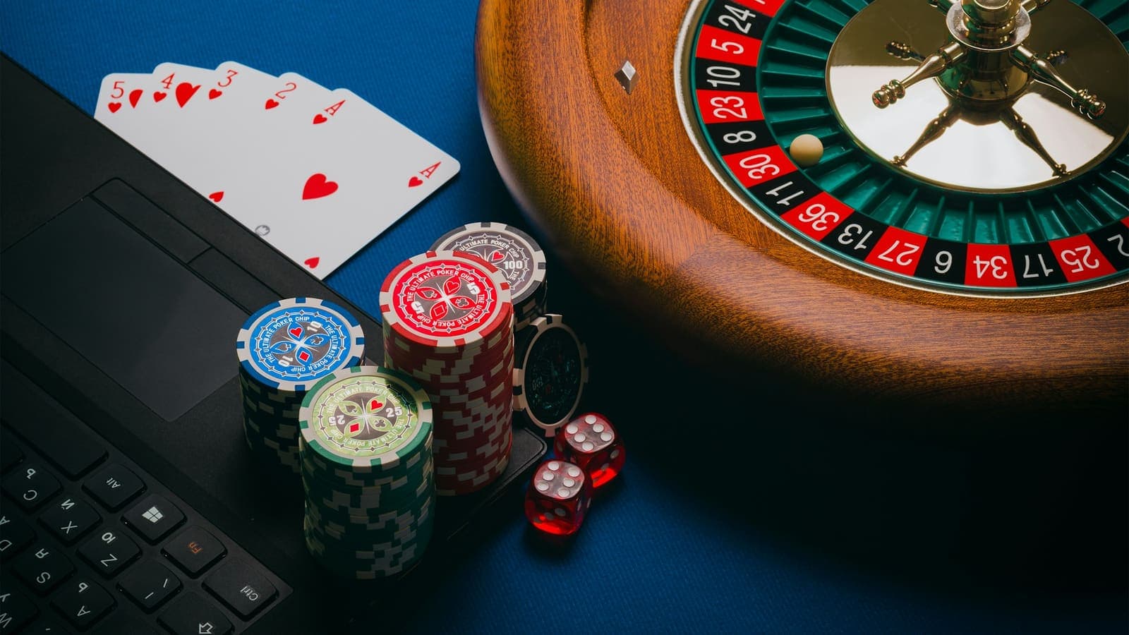 A roulette wheel, poker chips, cards and dice scattered on a laptop keyboard